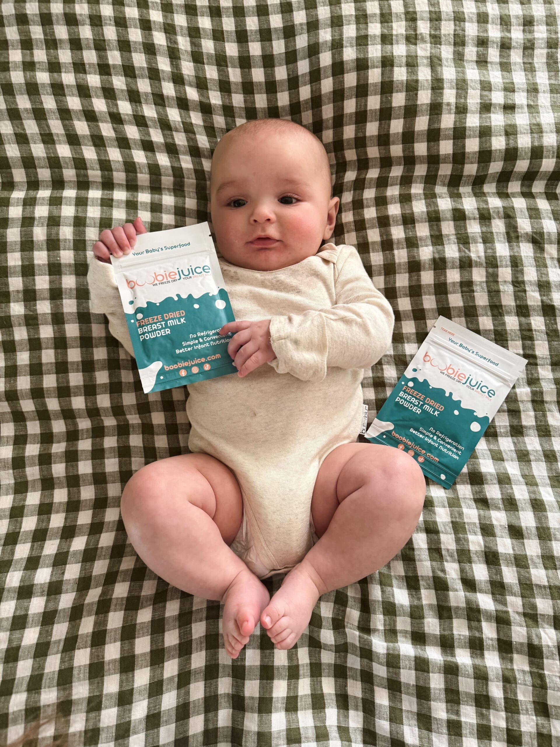 A baby on a bed holding a BoobieJuice pouch of freeze-dried breast milk powder.